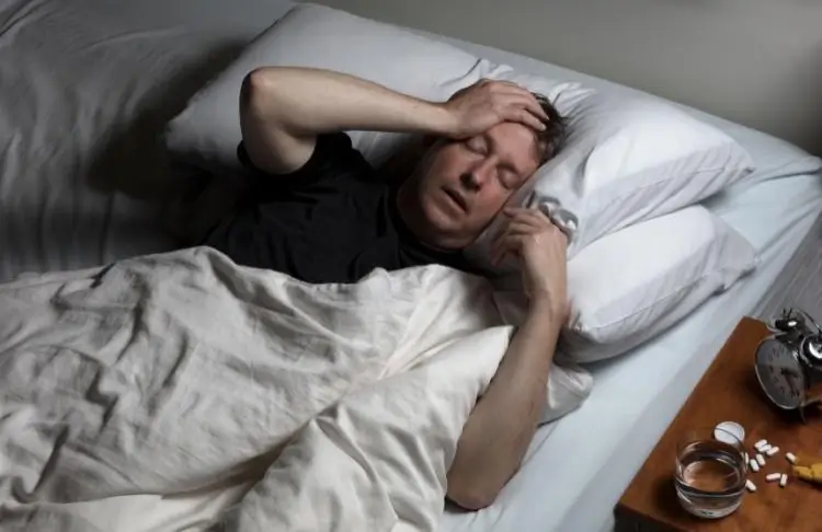 Person lying in bed holding head in discomfort, representing physical effects of fentanyl use
