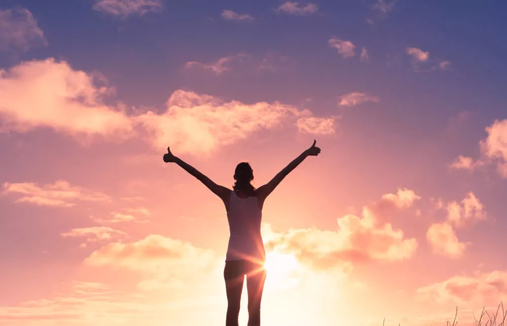 Person standing with arms raised at sunrise symbolizing hope, healing, and healthy coping skills in addiction recovery.