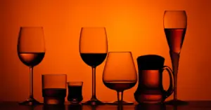 A variety of silhouettes including wine, beer, and liquor glasses against an amber background, representing the different forms of alcohol that affect brain chemistry.