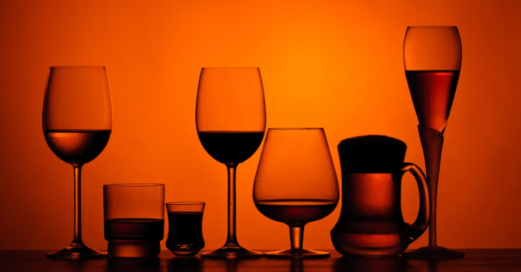 A variety of silhouettes including wine, beer, and liquor glasses against an amber background, representing the different forms of alcohol that affect brain chemistry.
