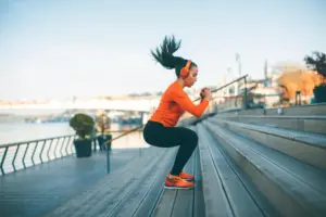 A woman in athletic wear performing jump squats outdoors, illustrating the physical activity often discussed in Adderall exercise safety guides.