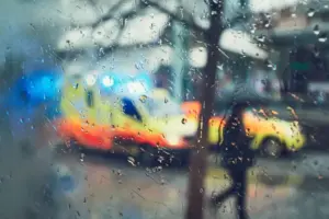 Blurred view of emergency ambulance lights through a rain-covered window representing overdose warning signs and urgent medical response