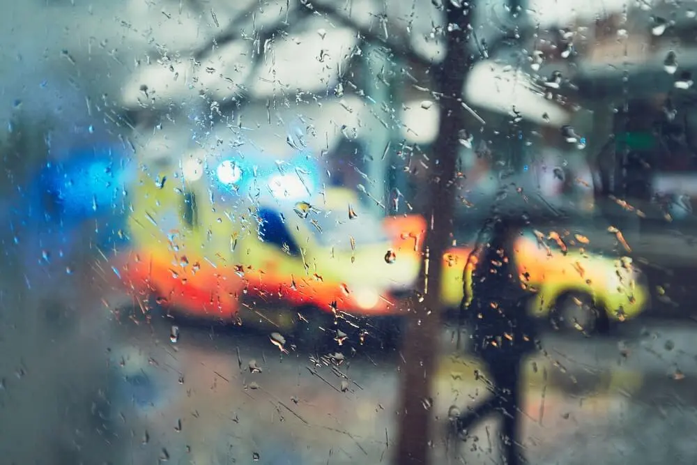 Blurred view of emergency ambulance lights through a rain-covered window representing overdose warning signs and urgent medical response