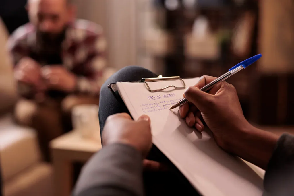 Therapist taking notes during an individual therapy session with a patient discussing addiction recovery.