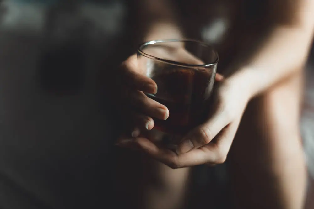 Close-up of a person holding a glass of alcohol while sitting, representing alcohol use disorder and problematic drinking