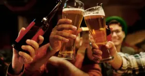 People holding and clinking beer glasses in a social setting, representing daily alcohol consumption and its potential health effects