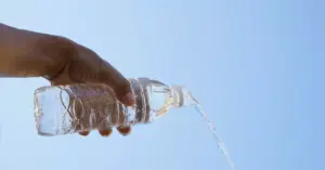 Person pouring water from a bottle to prevent dehydration caused by alcohol consumption.