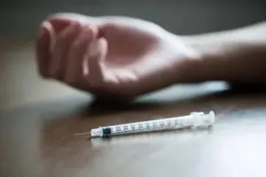 Syringe on table next to an unresponsive person’s hand, representing risks of meth use and possible allergic reaction