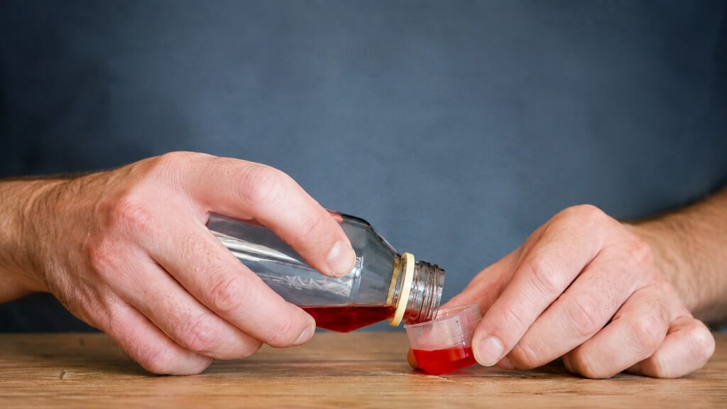 Person pouring cough syrup containing dextromethorphan (DXM), representing DXM misuse, withdrawal symptoms, and the need for professional detox treatment