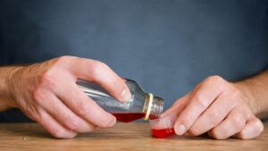 Person pouring cough syrup containing dextromethorphan (DXM), representing DXM misuse, withdrawal symptoms, and the need for professional detox treatment