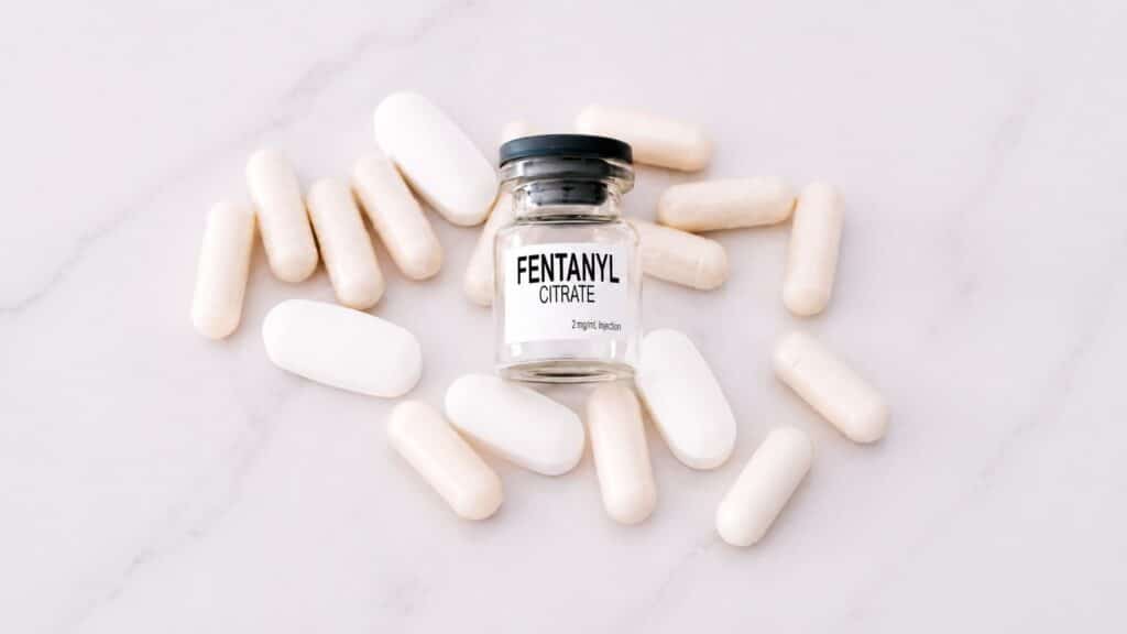 Bottle labeled fentanyl citrate surrounded by white pills representing the dangers of fentanyl addiction and overdose
