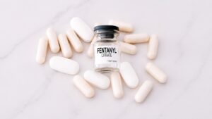 Bottle labeled fentanyl citrate surrounded by white pills representing the dangers of fentanyl addiction and overdose