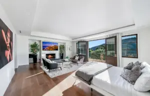 The image features a luxurious hotel-style bedroom designed for a wellness retreat, showcasing neutral tones and high-quality bedding. Large windows allow natural light to flood the space, complemented by elegant furnishings that create a peaceful and serene environment ideal for relaxation and rejuvenation.