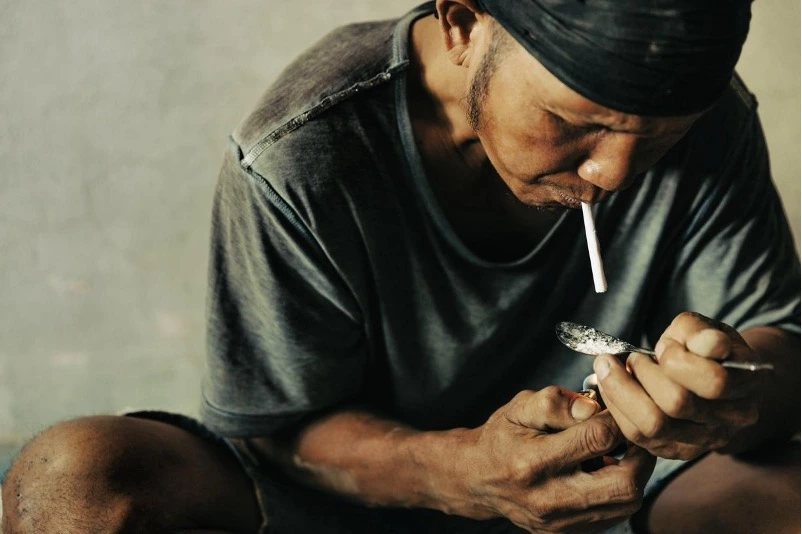 Meth Addiction Man burns meth on a spoon and inhales the vapors through a paper straw