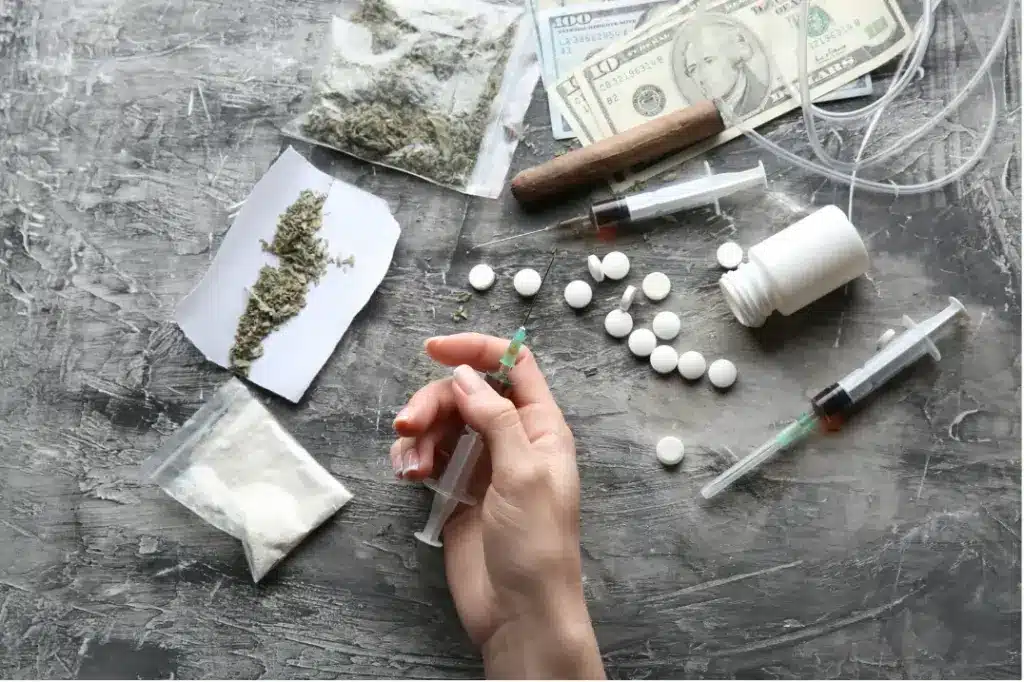 Drug paraphernalia, pills, syringes, cash, and cannabis displayed together, representing the risks of fentanyl-laced substances and polysubstance drug use.